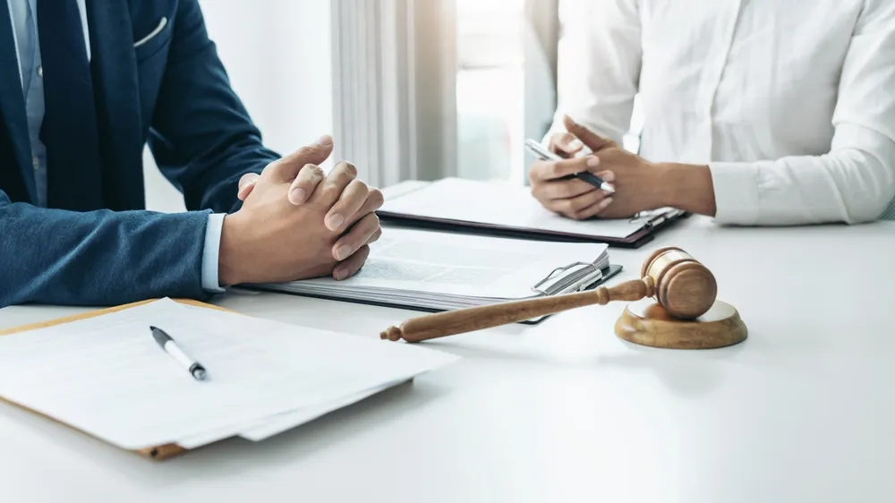 Two people in business attire sitting at a table with legal documents and a judge's gavel.