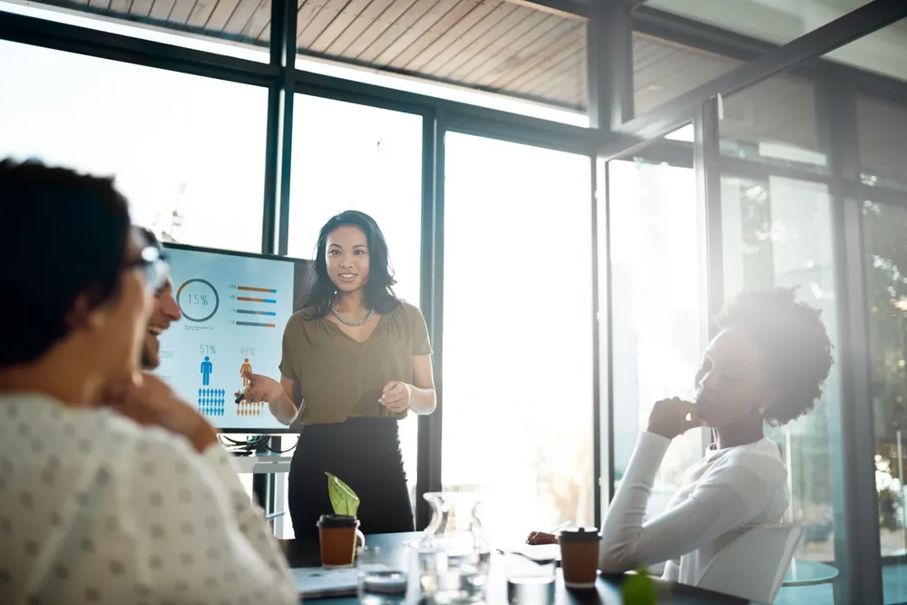 Woman presenting data on a screen to three attentive colleagues in a bright meeting room.