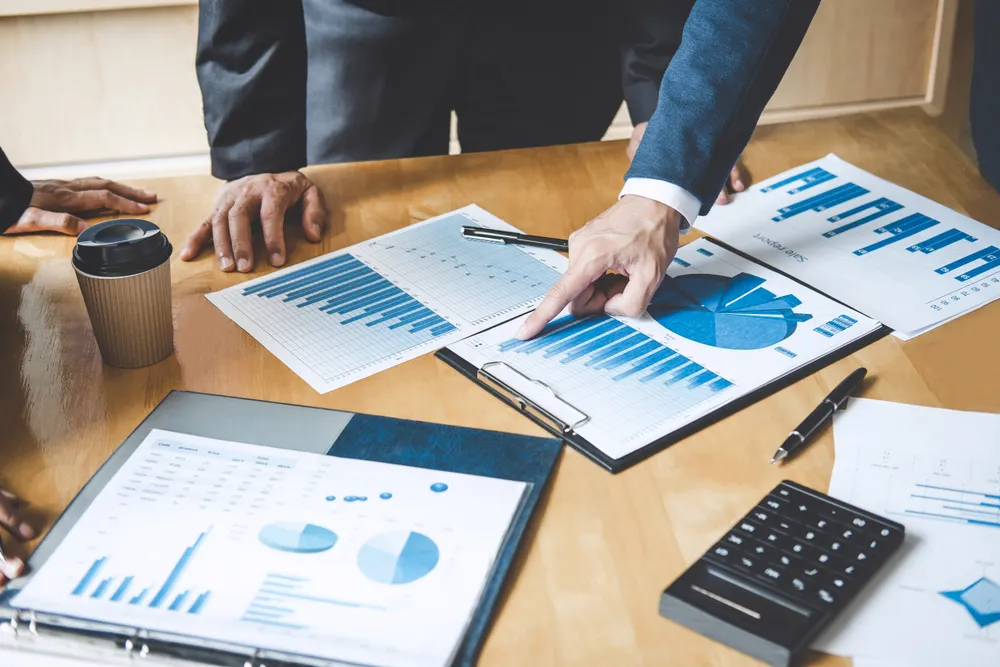 Business meeting with people discussing charts and graphs on papers and tablet at a wooden table.