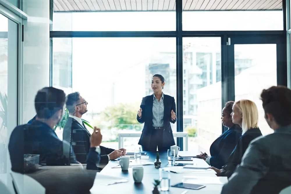 Businesswoman giving presentation to colleagues seated around conference table in modern office.
