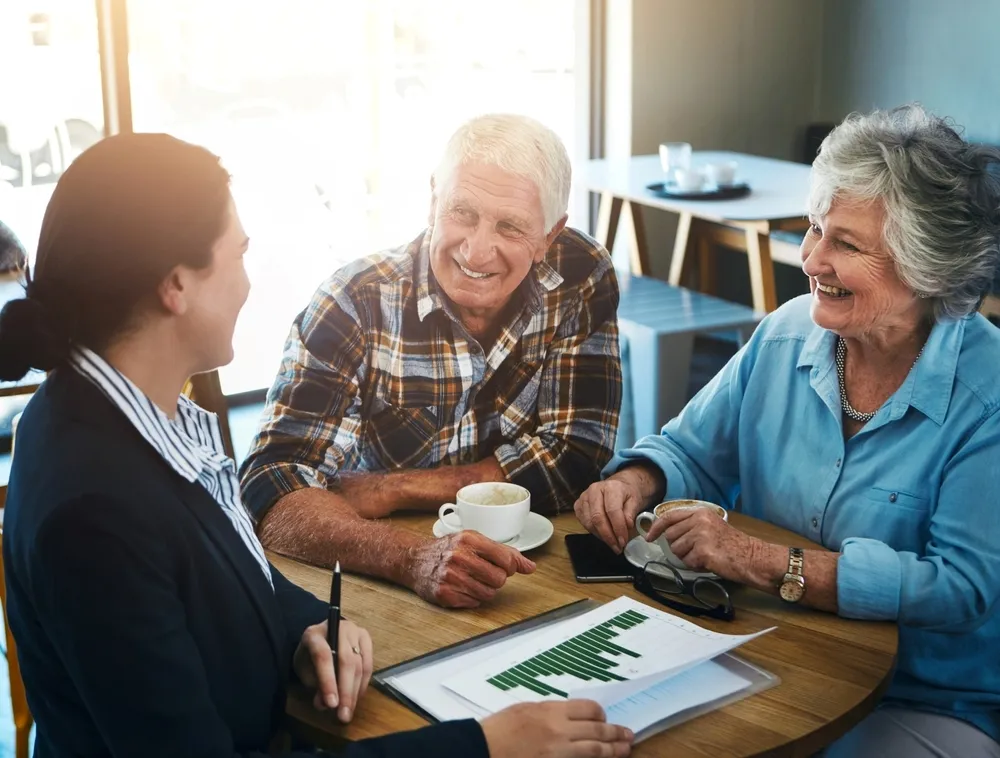 Senior couple meeting with advisor at a table with coffee and financial documents.