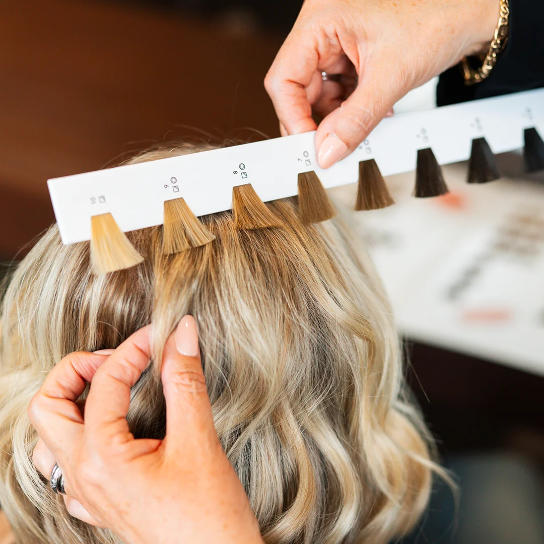 Hand comparing blonde hair with color swatches to match hair dye shade.