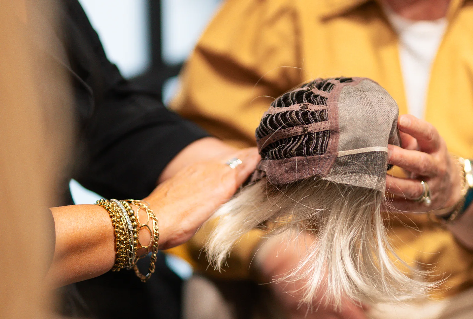Twee mensen houden een haarwerk met binnenzijde en lichtblonde haren vast.