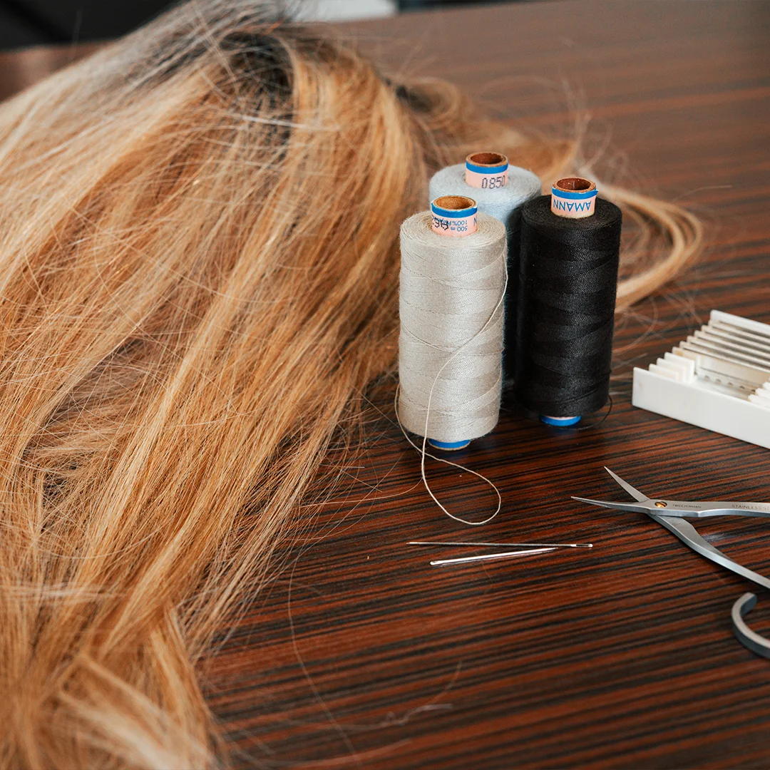 Lichtbruin haar, drie garenklossen, twee naalden, schaar en kam op houten tafel.