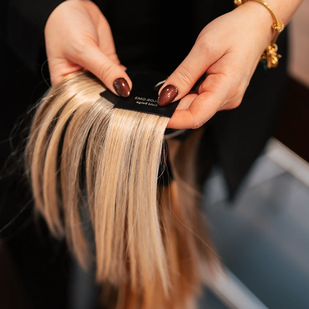 Hand met donkergelakte nagels houdt kleurstaal met diverse blondtinten haarstrengen vast.