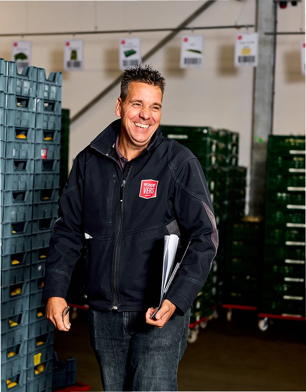 Lachende medewerker van Heerkens Vers tussen de groene kratten