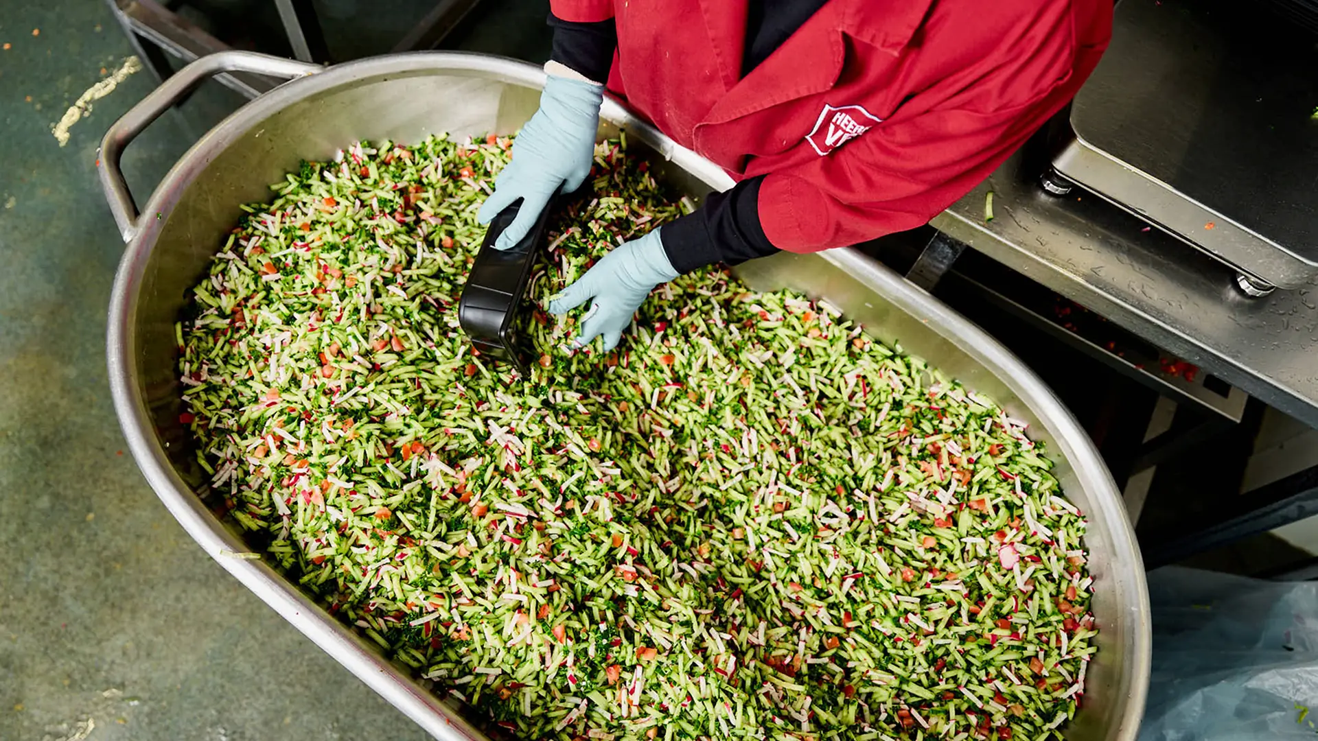 Handen in handschoenen mengen een gesneden groentemix in een grote pan
