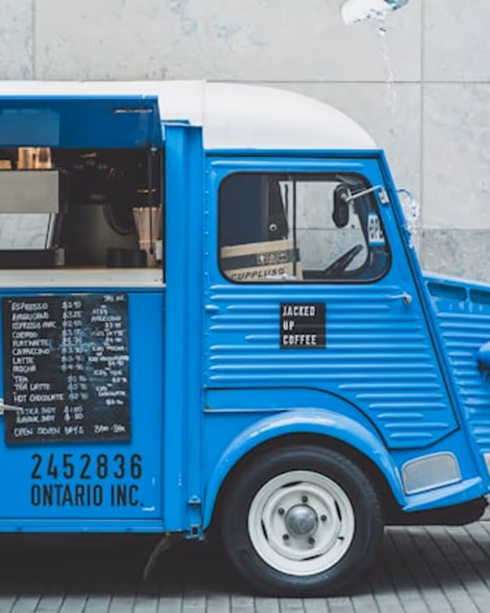 Un camion de café bleu vintage stationné avec menu de boissons sur le côté et texte 'Jacked Up Coffee'.
