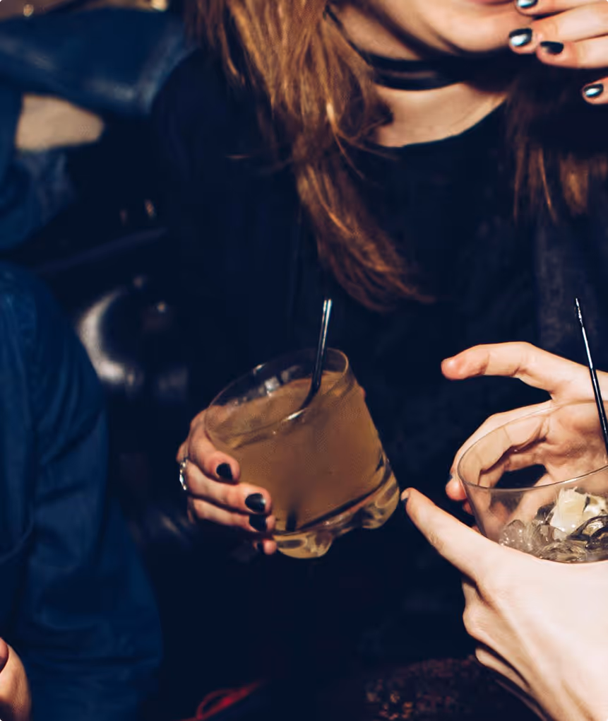 Deux personnes tenant des verres avec boissons et glaçons dans un cadre sombre et social.