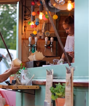 Un stand de crème glacée avec une serveuse et différentes boules de glace colorées en arrière-plan.