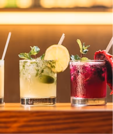 Plusieurs cocktails colorés garnis de feuilles de menthe, rondelles de citron et tranches de fruit rouge.