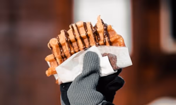 Une main gantée tient une gauffre avec du chocolat fondu dessus.