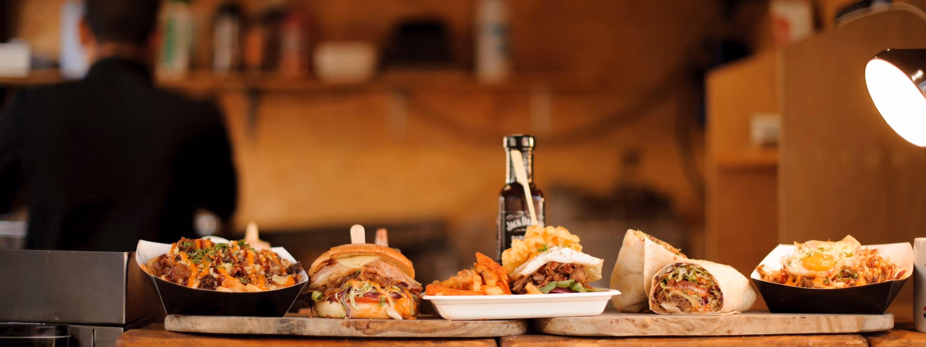 Divers repas de restauration rapide : burger, frites, wrap, et plats garnis présentés sur une table en bois.