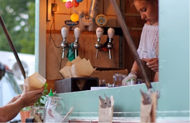 Une femme sert une personne au comptoir d'un food truck avec des tireuses de bière en arrière-plan.