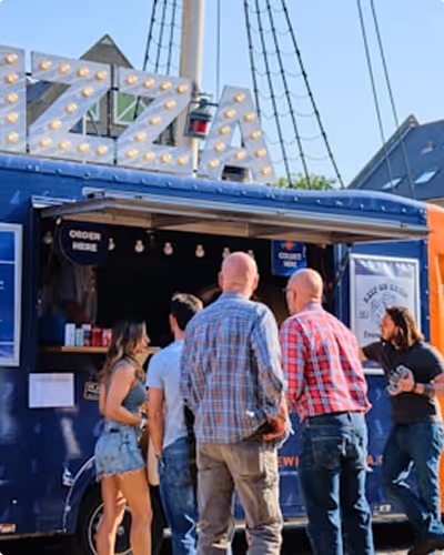 Un groupe de personnes attend à un food truck bleu sous un panneau lumineux.