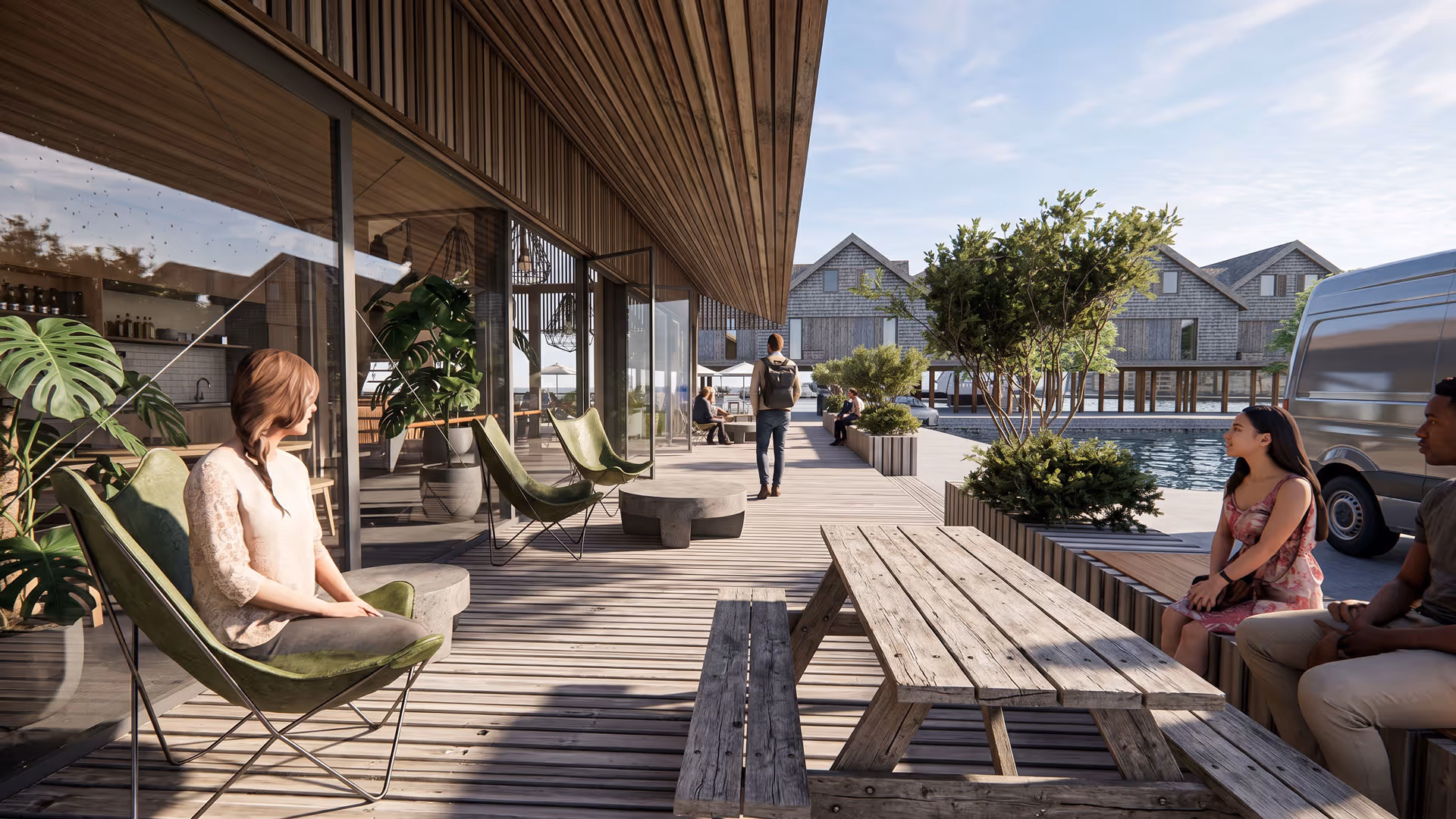Buiten loungegedeelte met houten terras, groene stoelen, planten en mensen die ontspannen bij een waterpartij met huizen op de achtergrond.