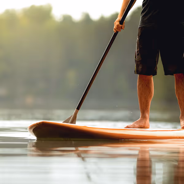 Persoon staat op een paddleboard en peddelt op rustig water met bos op de achtergrond.