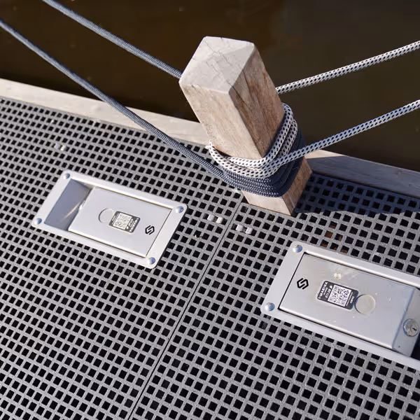 Houten paal op een metalen roosterdek met twee vastgemaakte witte touwen bij het water.
