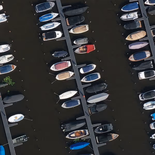 Luchtfoto van een jachthaven met verschillende kleine boten afgemeerd aan steigers op rustige wateren.