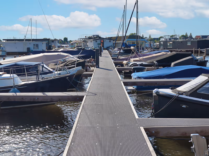 Houten steiger tussen boten in een jachthaven onder een blauwe lucht met enkele wolken.