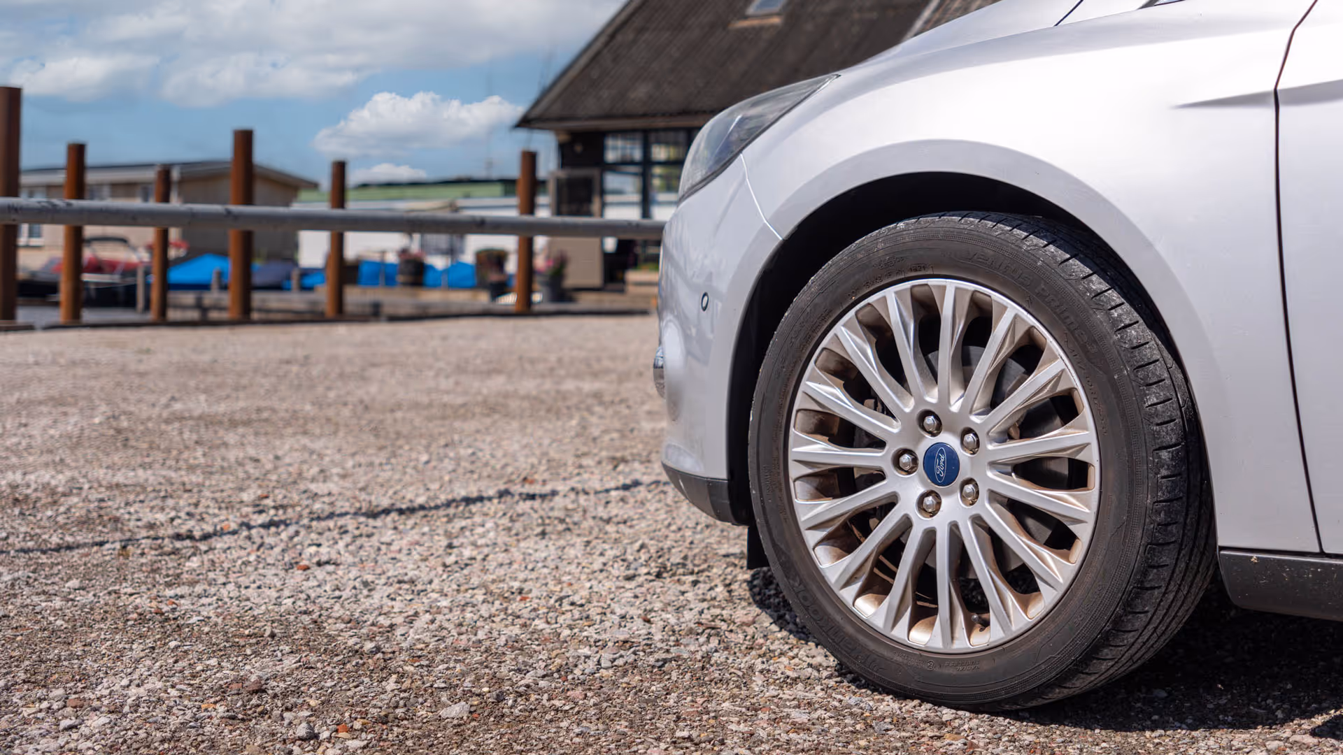 Close-up van een voorwiel van een zilveren Ford geparkeerd op grind.