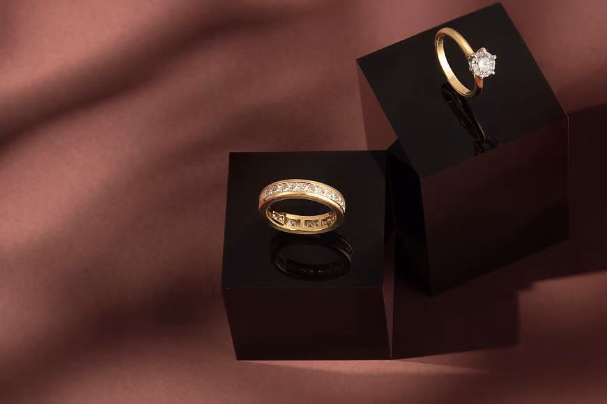 18K Yellow Gold Half Eternity Ring with Princess Cut Diamonds & Certificated Tiffany and Co. 18K Yellow Gold Solitaire Diamond Ring on a dusky pink background