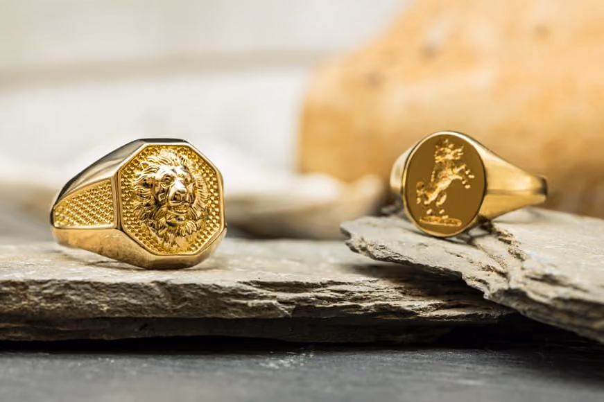 Two yellow gold signet rings embossed with designs of a wolf/dog and a lion, sat upon slate