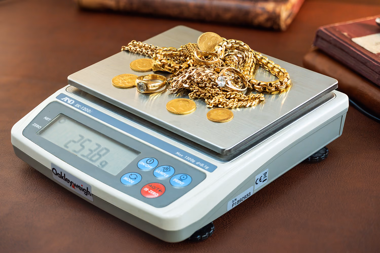 Digital scale weighing assorted gold jewelry and gold coins, showing a weight of 25.38 grams.