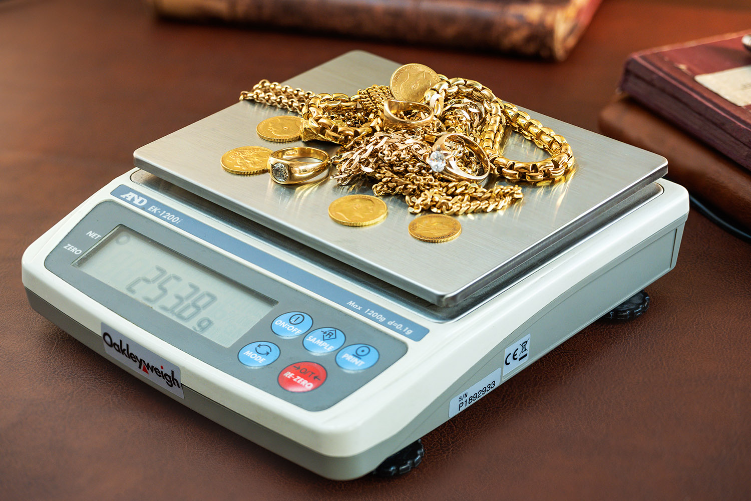 Digital scale weighing assorted gold jewelry and gold coins, showing a weight of 25.38 grams.