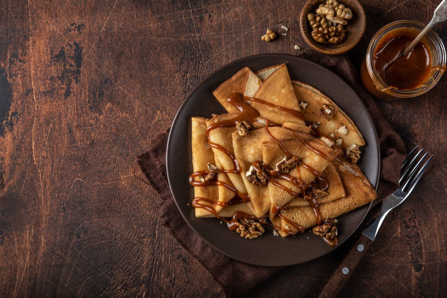 Plate of folded crepes drizzled with caramel sauce and garnished with walnut pieces on a rustic wooden table.