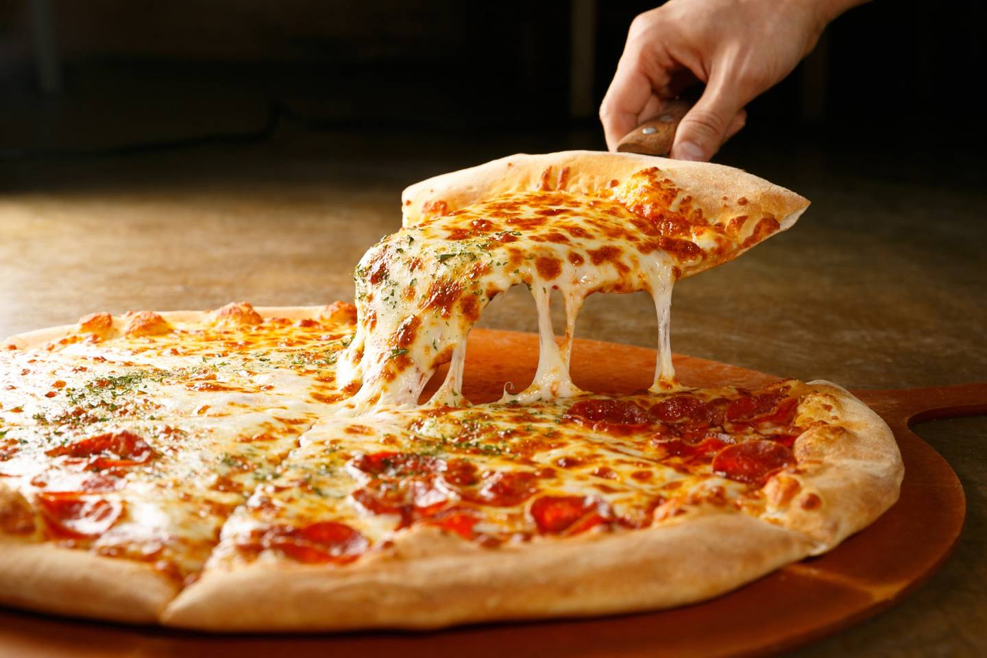 Hand lifting a slice of pepperoni pizza with melted cheese stretching from the slice.