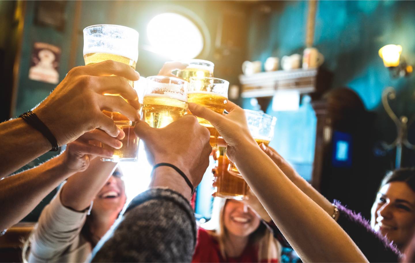 Group of friends raising glasses of beer in a toast in a warmly lit pub.