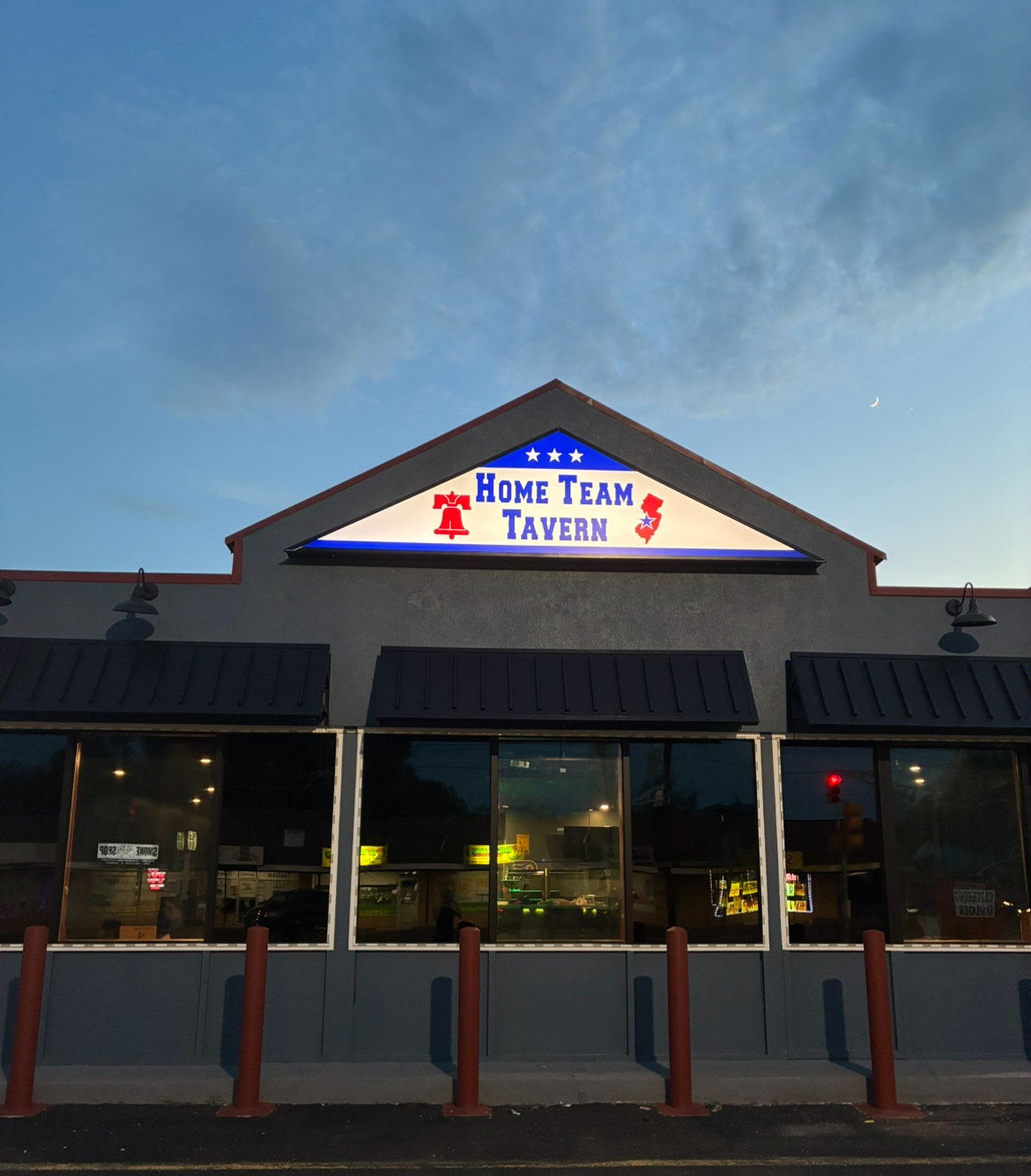 Outdoor seating area with black metal tables and chairs under blue and beige umbrellas outside a blue and white sandwich shop.