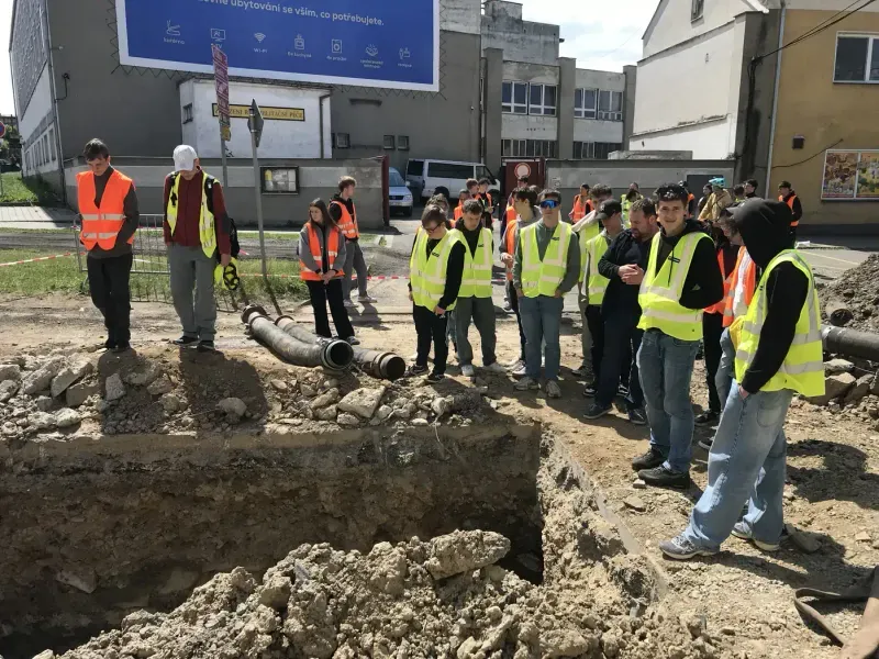 Studenti poslouchají výklad na staveništi během odborné exkurze.