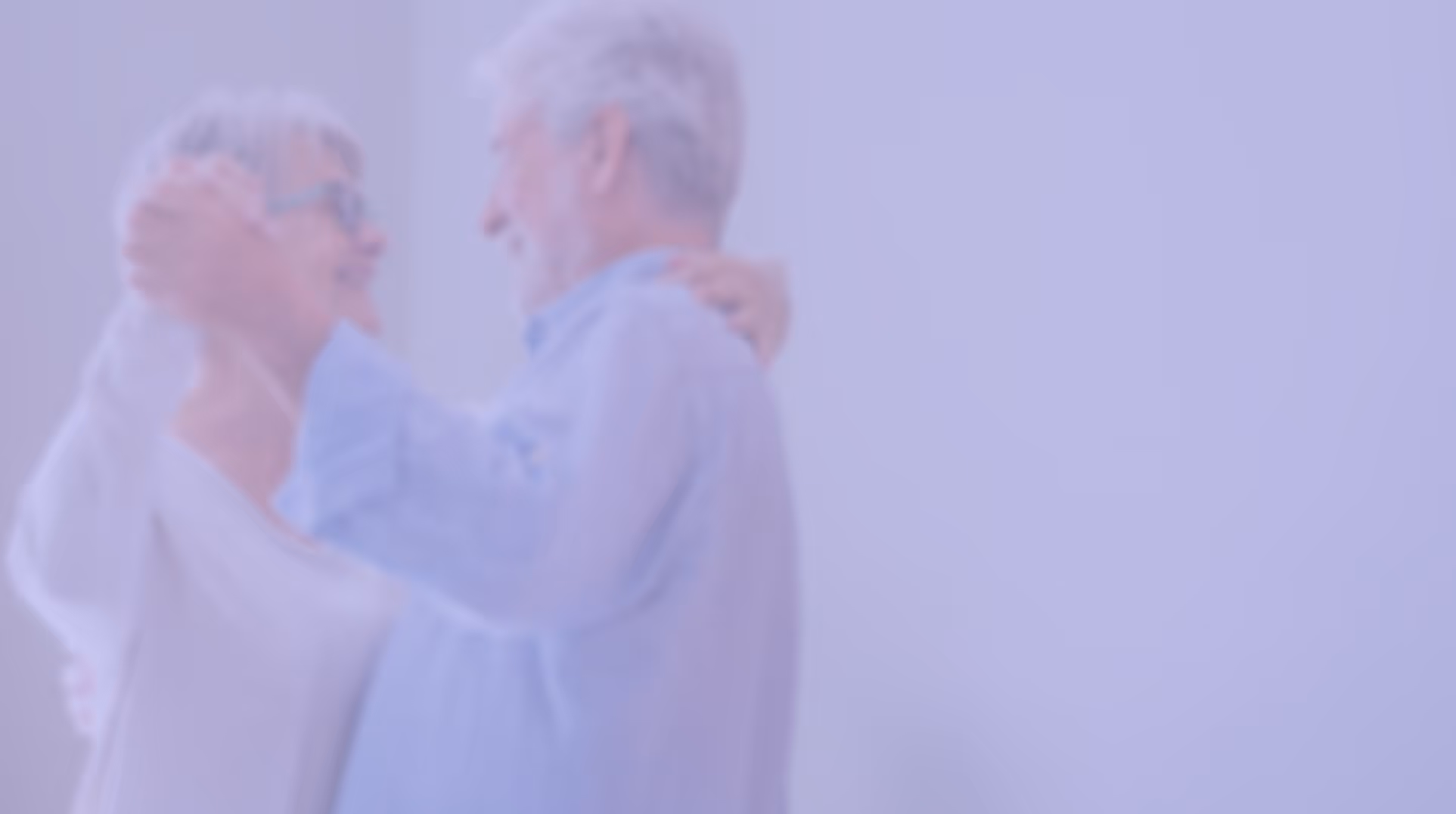 Elderly couple smiling and dancing together in a softly lit room.