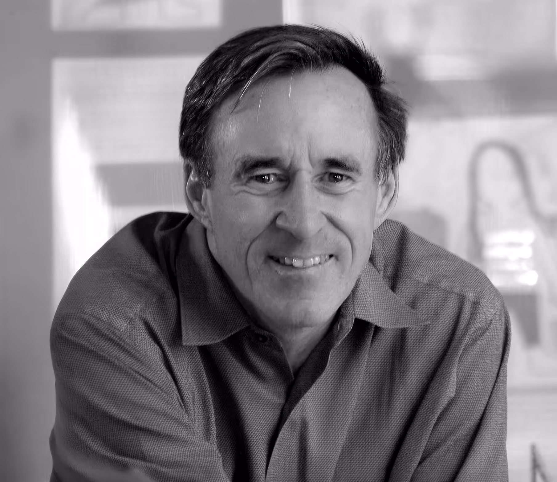 Smiling middle-aged man in a collared shirt looking directly at the camera in a softly lit room.
