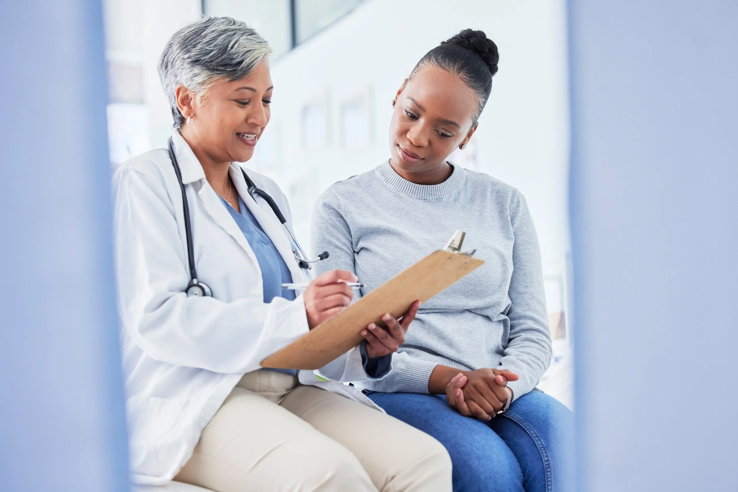 Doctor with a stethoscope showing clipboard notes to a female patient during a consultation.