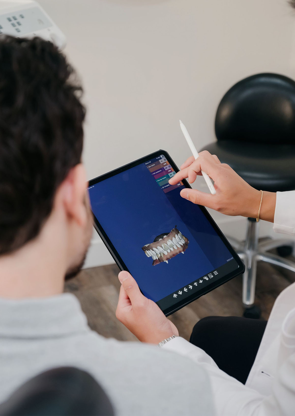 Person holding a tablet showing a 3D dental model while another points on the screen with a stylus.