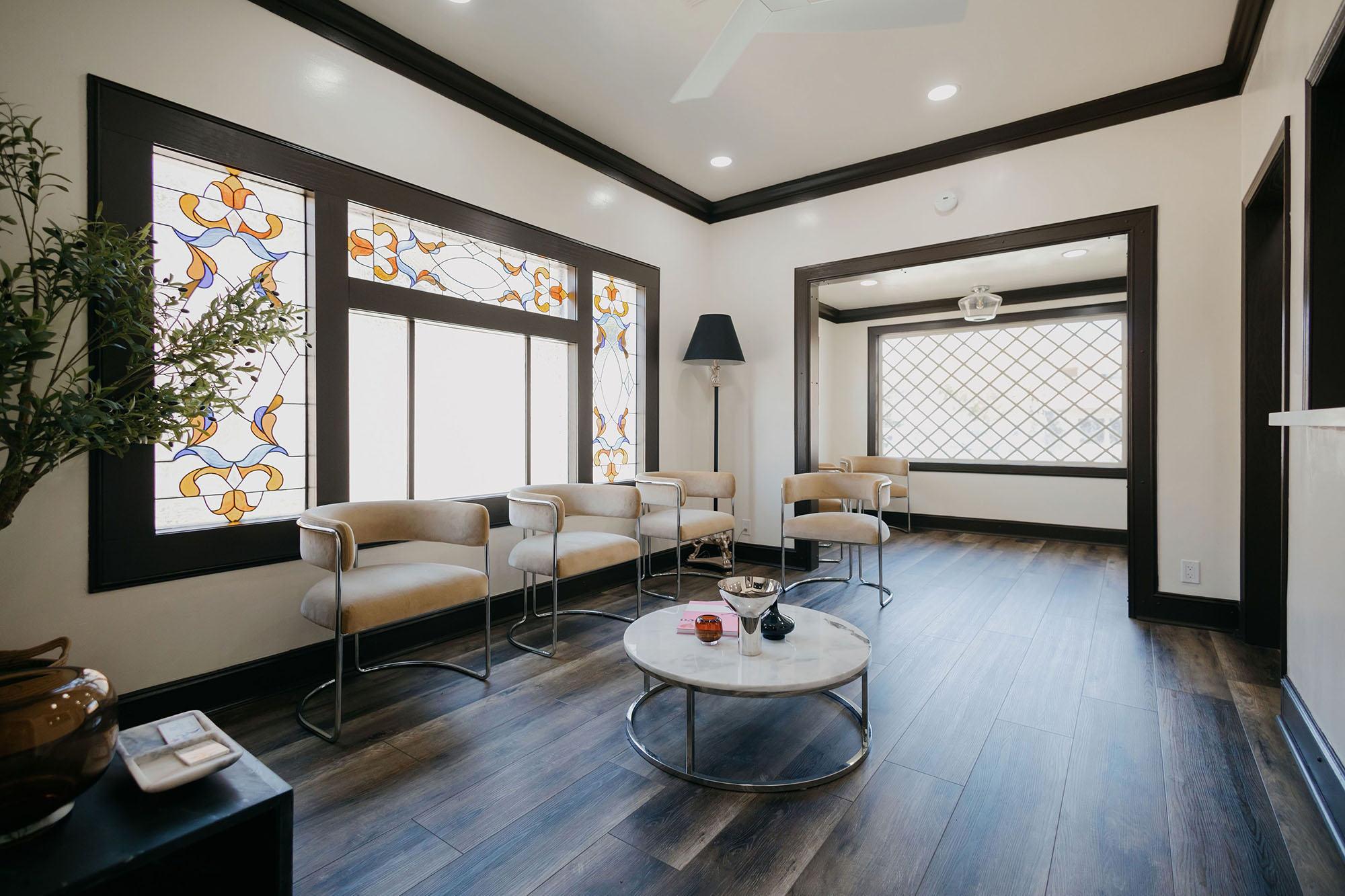 Modern room with four beige chairs, stained glass window, round marble table, and wooden floor.