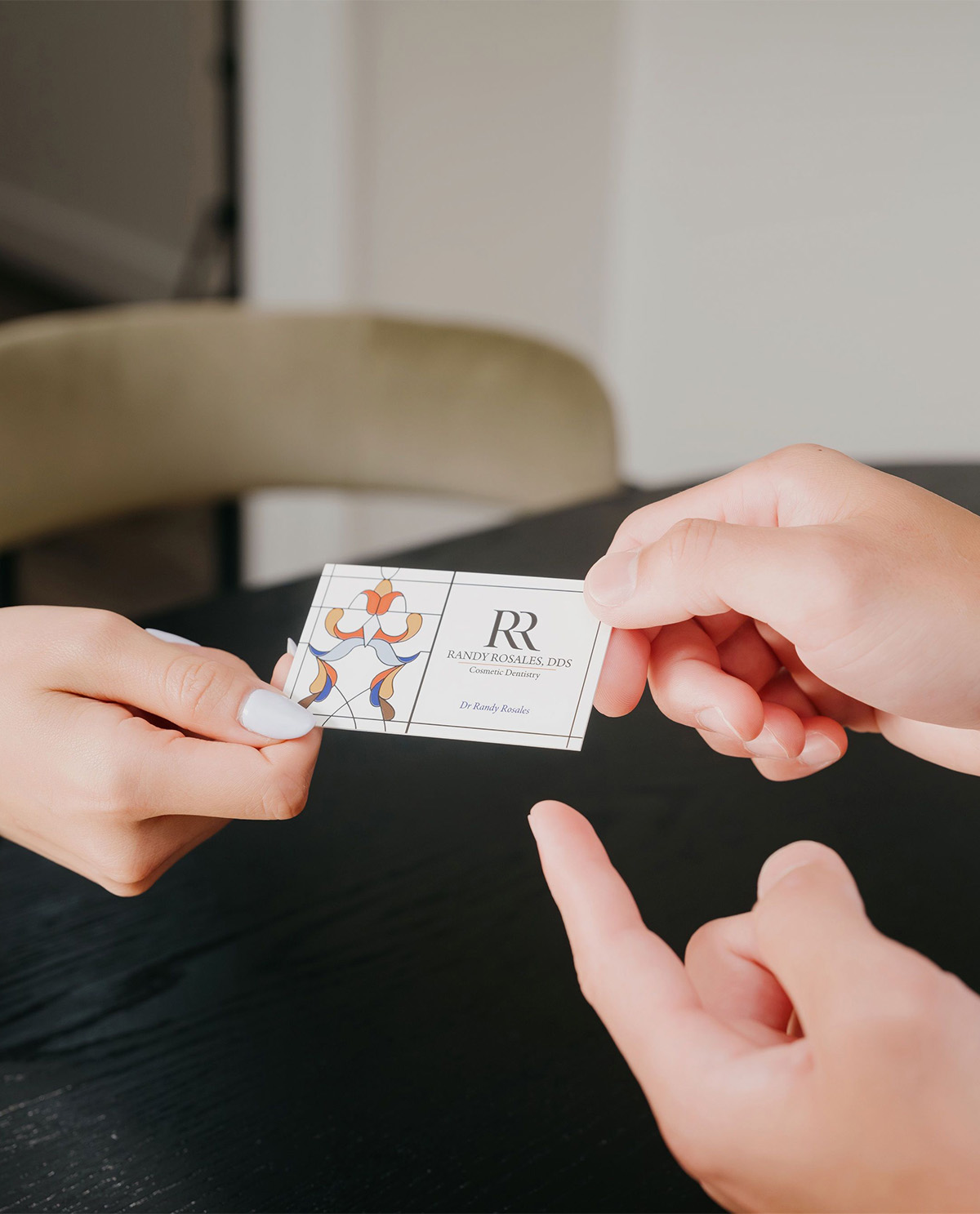 Two hands exchanging a business card for Randy Rosales, DDS, cosmetic dentistry with colorful design.