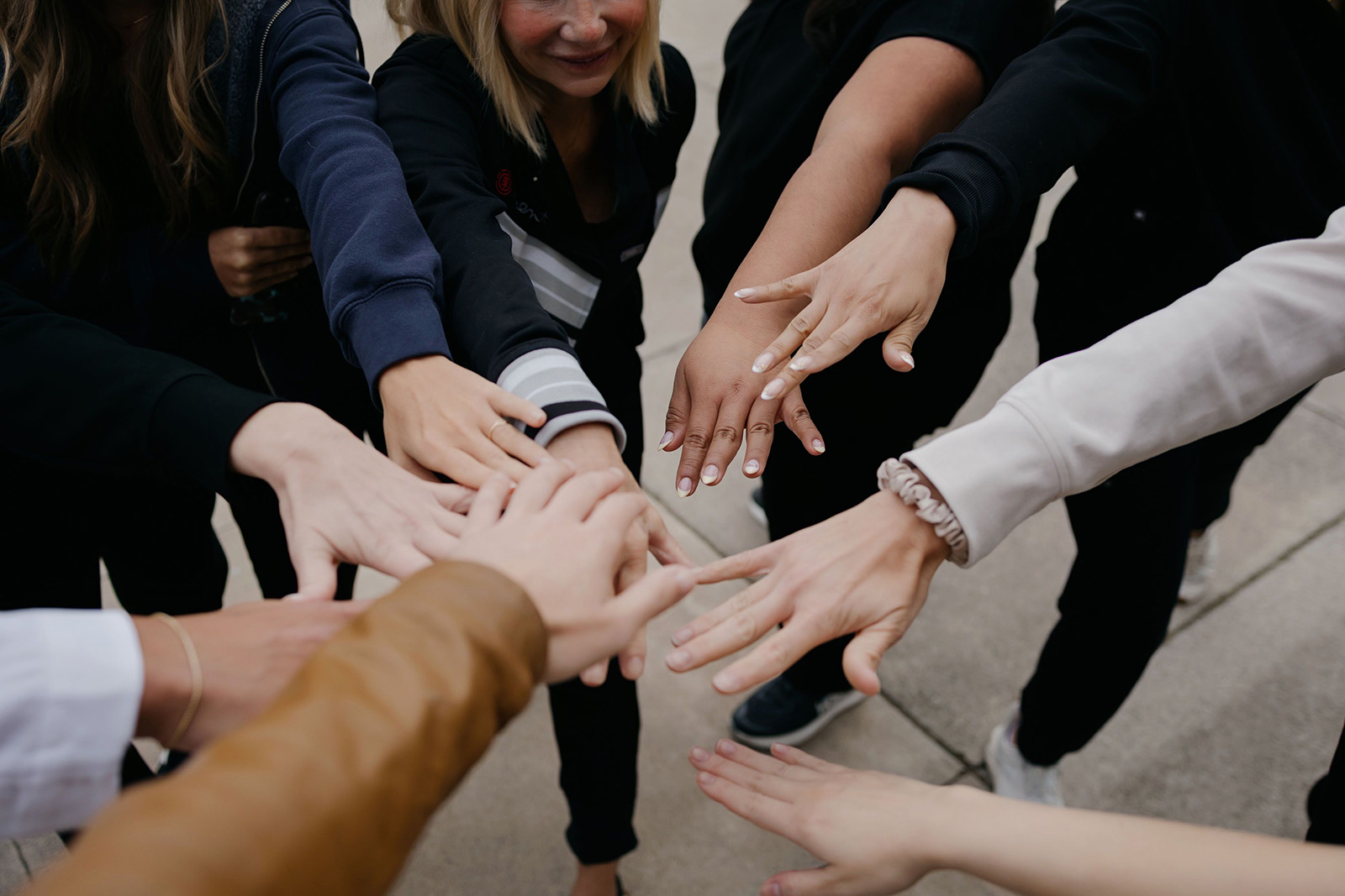 Group of people standing in a circle with hands stacked together in the center outdoors.