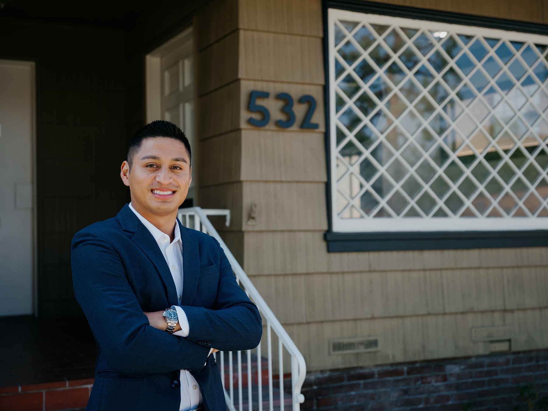 Man in blue suit and white shirt standing with arms crossed in front of house number 532.