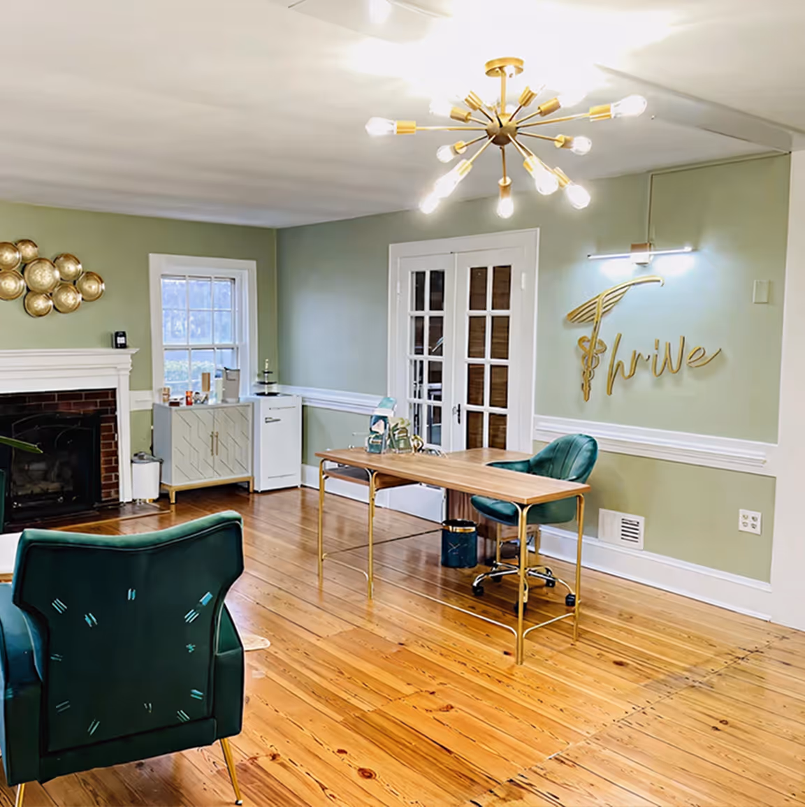 Bright office with green chairs, wooden floor, a table, fireplace, and 'Thrive' wall art.