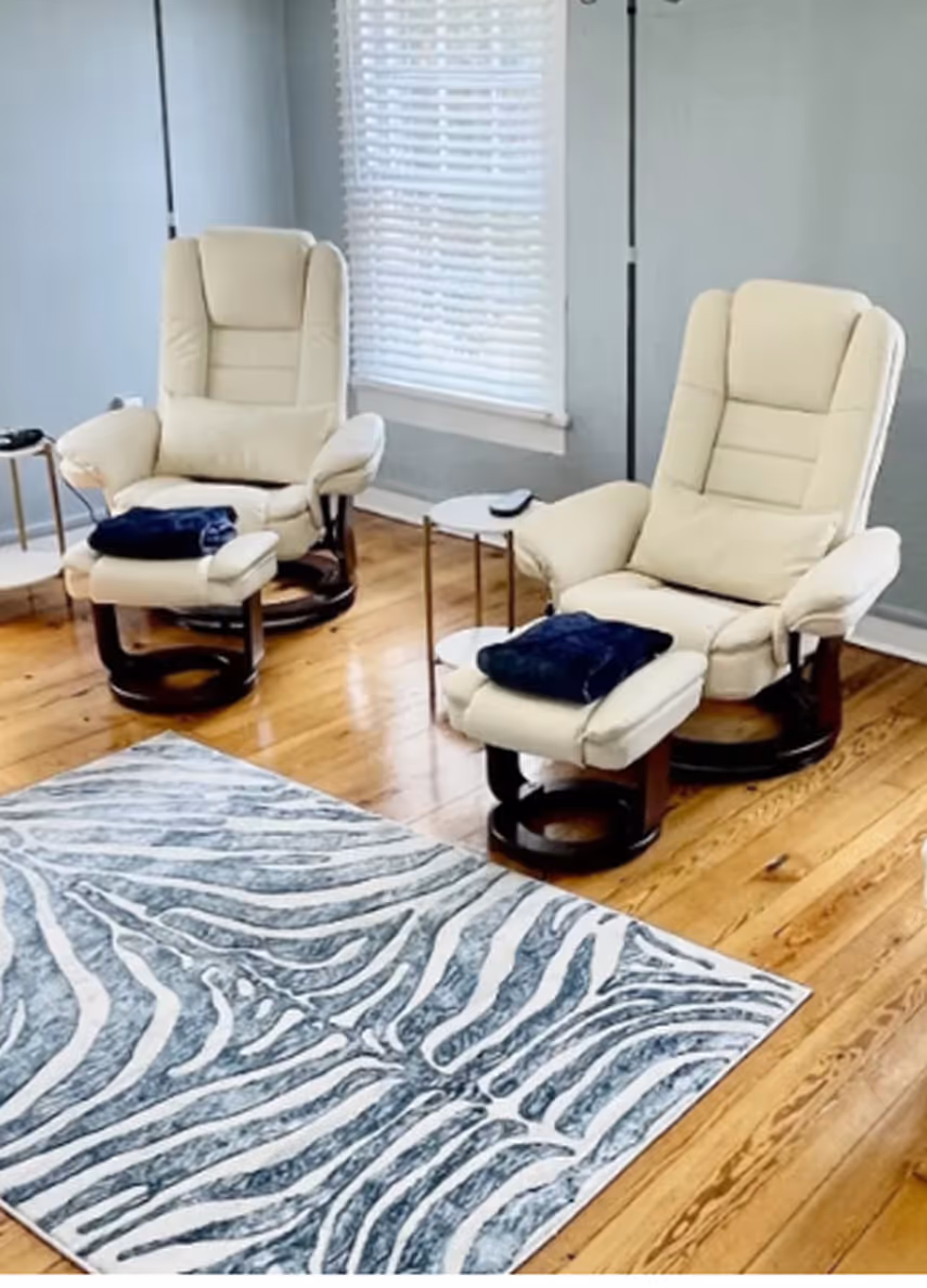 Two cream recliner chairs with footrests and navy blankets in a room with wood floor and zebra-print rug.