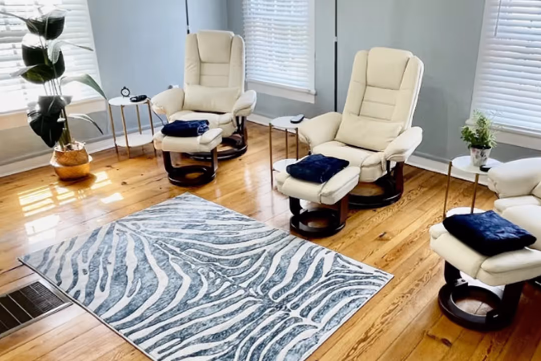 Living room with three beige reclining chairs, zebra pattern rug, wooden floor, and side tables with plants.