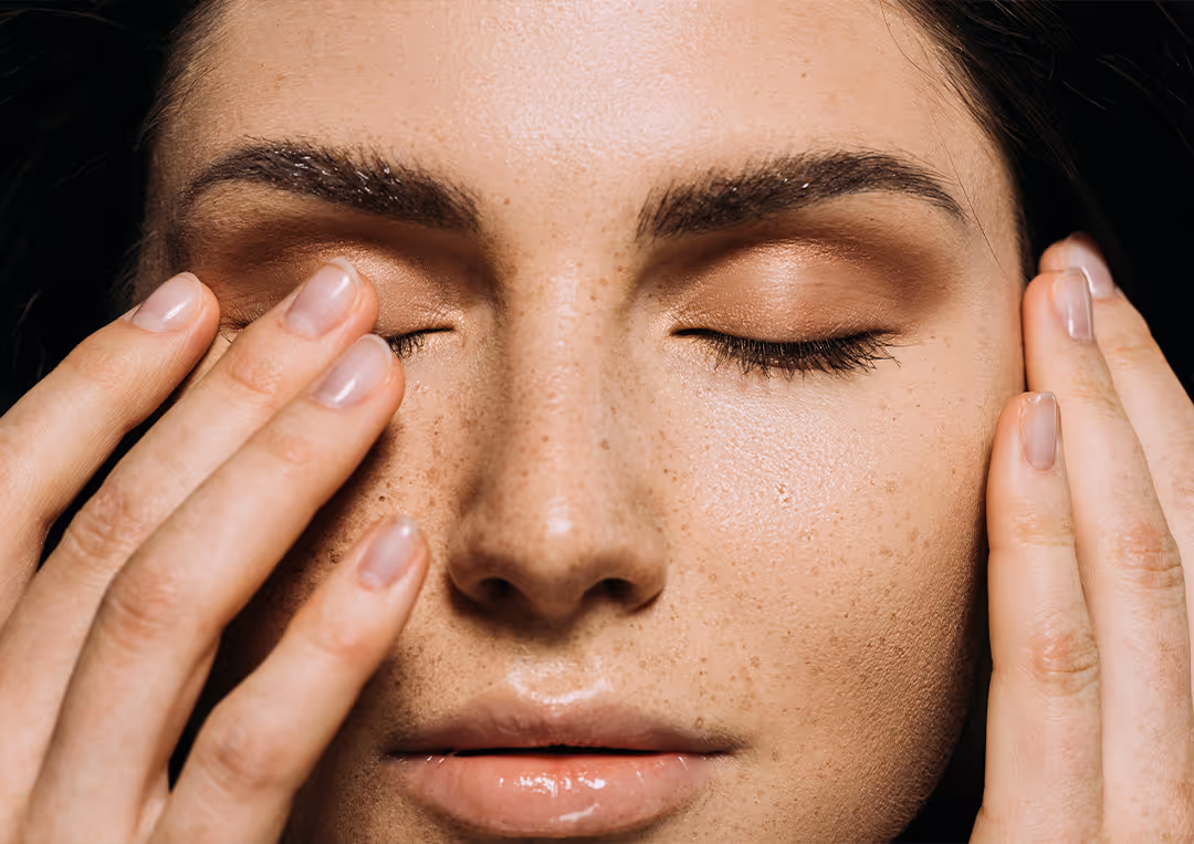 Close-up of a woman with freckles touching her closed eyes with her fingers.