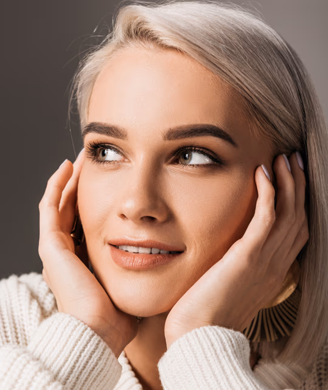 Close-up of a woman with platinum blonde hair resting her face in her hands, looking to the side.