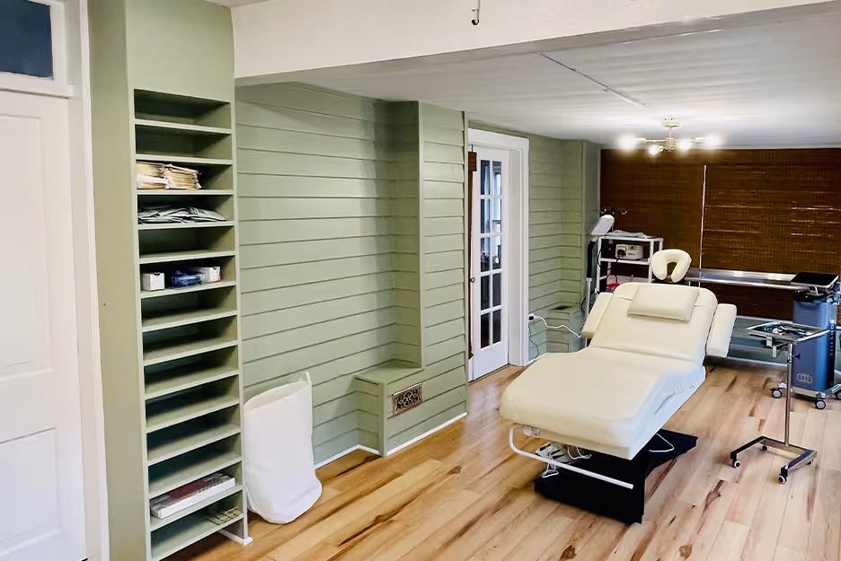 Treatment room with reclining white medical chair, green paneled walls, and wooden floor.