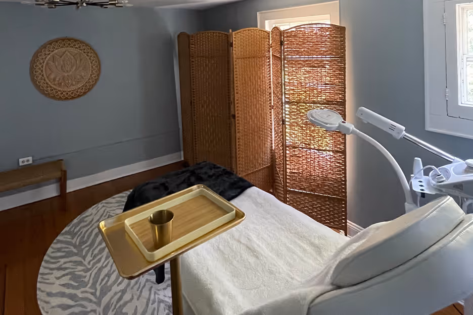 Cozy treatment room with white recliner, gold tray, wicker screen, and wall decor on blue walls.