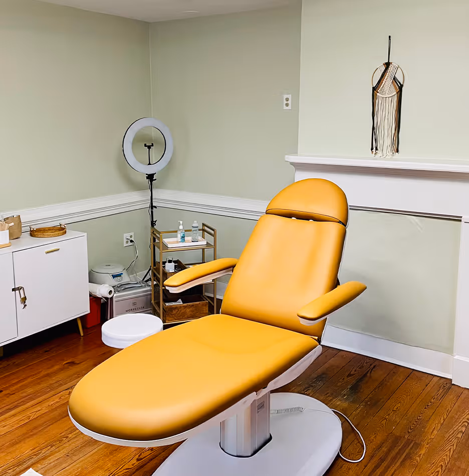 Modern yellow reclining chair in a clean treatment room with hardwood floors and soft green walls.